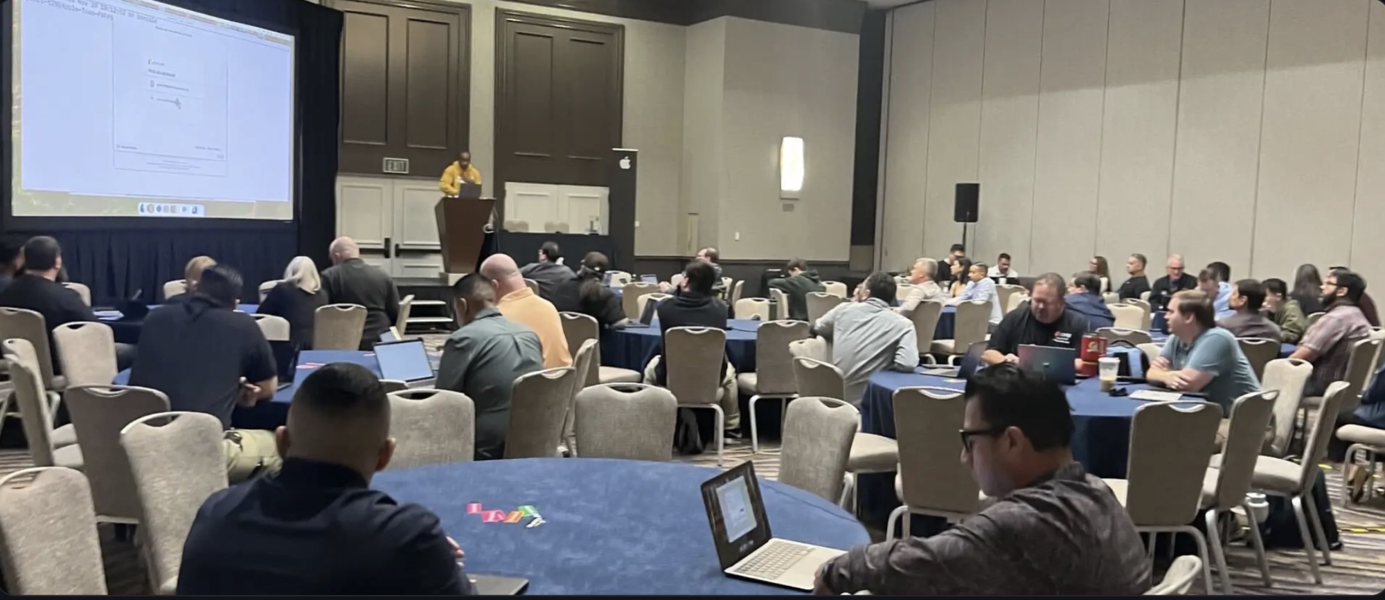 Kenan presenting at the front of a full conference ballroom